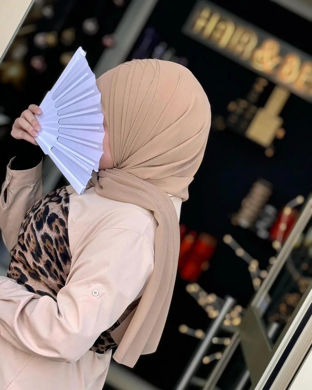 Schlichter beiger Hijab mit Salonschild Hair and Beauty im Hintergrund